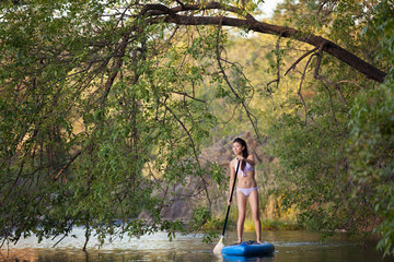 A young, asian, woman enjoying an SUP trip down a river on a paddle board.