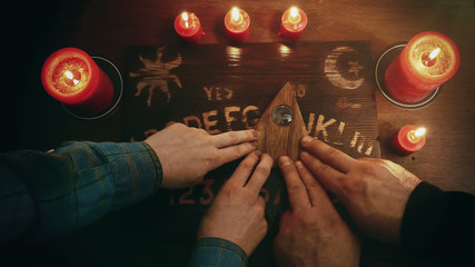 Two people conducting a seance using a Ouija Board, or Talking Spirit Board, with red candles. Shot...