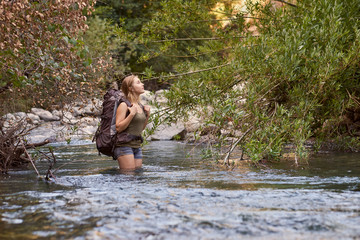 A female hiker crossing a creek with a backpack while exploring the Sierra Nevada Mountains of Northern California
