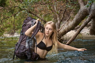 A female hiker in waist deep water holding her backpack above the water as she crosses a mountain creek.