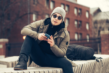 Handsome student man texting on cell phone sitting on the bench wearing casual clothes