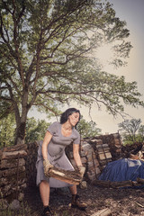 A pregnant woman in boots and a vintage dress stacking wood on a rural ranch in Northern California.