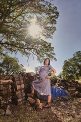 A pregnant woman in a dress and boots resting after stacking wood on a pile.