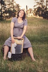 Pregnant in a dress while washing clothes on a washboard in the summer.