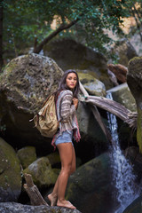 Tennage girl with a backpack standing next to a waterfall in the Sierra Nevada Mountains of Northern California.