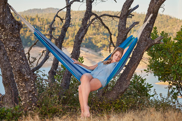 A barefoot woman resting in a hammock on a hill above a mountain lake in Northern California.