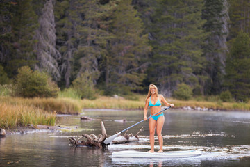 A young woman on using a paddle board on a small river in the middle of a forest in the mountains of Northern California,