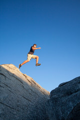 A young man outdoors leaping from one boulder to another in the Sierra Nevada Mountains of Northern California.