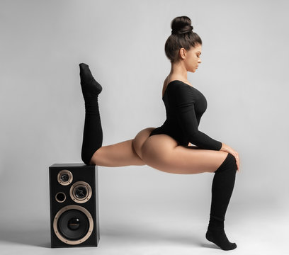 Beautiful brunette woman in black bodysuit sits and leans on a music speaker.