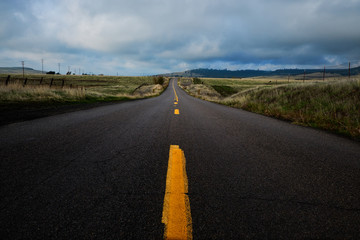 A rural country road passing through ranch land with storm clouds overhead.
