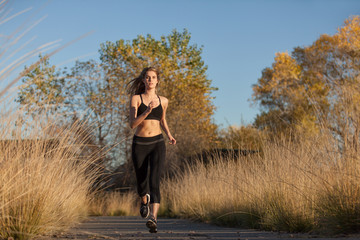 A young woman in black work out clothing jogging on an outdoor running trail.