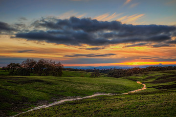 A stream passing through a green field with a sunset in the background on Table Mountain in Northern California.