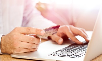 Closeup of a Man Typing on a Laptop and Holding a Credit Card
