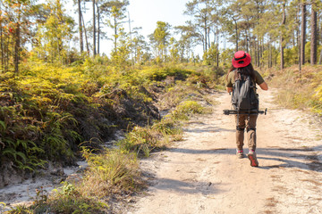 Obraz premium Woman traveler with backpack holding hat alone on dirt road at tropical forest. Female photographer outdoors in nature. Travel holiday relaxation conceptt, space for text,