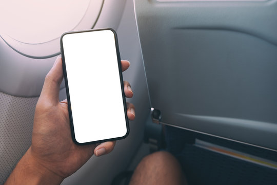 Mockup image of a hand holding a black smart phone with blank desktop screen next to an airplane window
