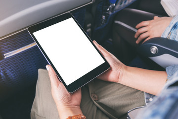 Mockup image of a woman holding and looking at black tablet pc with blank white desktop screen while sitting in the cabin