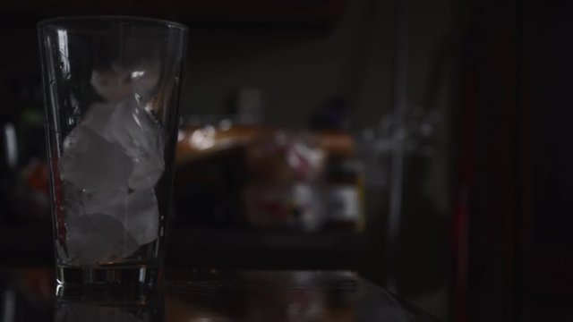 Ice cubes being dropped into a glass sitting on a countertop