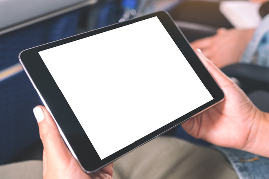 Mockup image of a woman holding and looking at black tablet pc with blank white desktop screen while sitting in the cabin