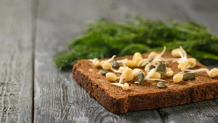 A bunch of dill and bread with sprouted mung beans and pumpkin seeds on a wooden table.