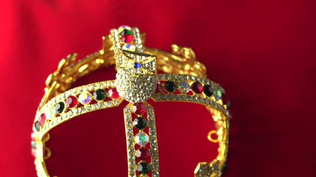 Gold crown with luxury color jewels and diamonds, view from above. With reflection and lights sparks. Slow rotation on the red royal color surface. 4k, uhd.