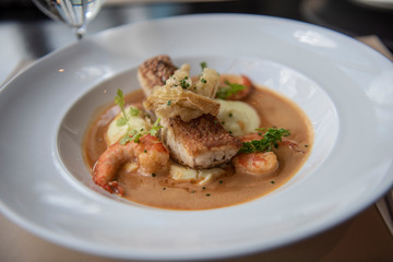 Fresh sea food menu with red snapper, shrimp, potato and topped with brown gravy. Served on a round white plate as a main course in a modern French restaurant in Bangkok, Thailand.