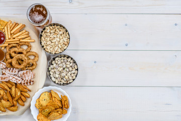 Mix of snacks with beer on light wooden background. Top view, Empty space for text