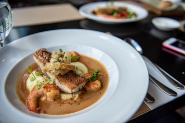 Fresh sea food menu with red snapper, shrimp, potato and topped with brown gravy. Served on a round white plate as a main course in a modern French restaurant in Bangkok, Thailand.