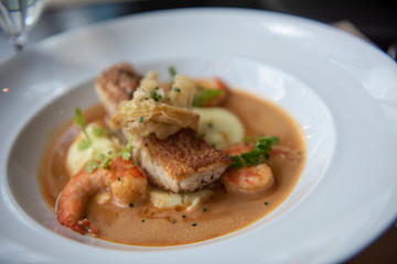 Fresh sea food menu with red snapper, shrimp, potato and topped with brown gravy. Served on a round white plate as a main course in a modern French restaurant in Bangkok, Thailand.