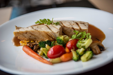 A grilled chicken served with broccoli, red tomato, carrot, mushroom and corn in Asian style. Served as a main course in a modern French restaurant in Bangkok, Thailand.