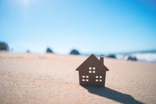 Small home model on sand beach with blue sky background.