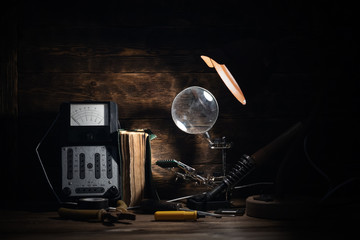 Retro analog voltmeter, soldering iron,handbook, microcircuit, pliers and screwdriver in the light of lamp on a brown wooden table background. Electrical works abstract background.