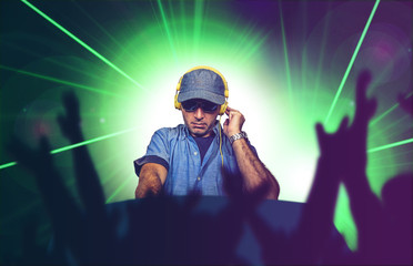 young happy and cool deejay playing music at party event in night club mixing techno songs on laser...