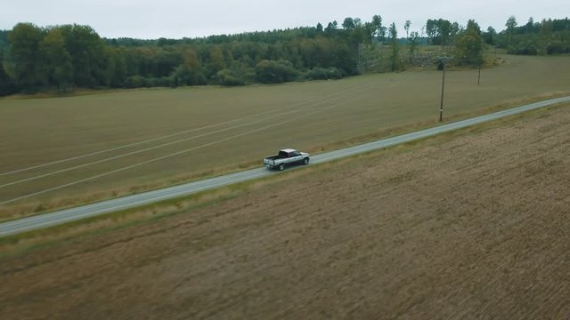 Aerial drone footage of a car driving on a gravel road, panning with the speed of the car and coing over electricity cords while birds are flying by.