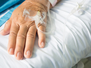 Close up old woman patient hand and iv set for fluid intravenous drop saline drip on white hospital bed background in the hospital room.Medical treatment emergency patient.Seriously patient admitted.