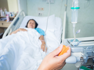 Close up nurse hand adjust set iv fluid intravenous drop saline drip in hospital room with blurry patient woman on hospital bed.Medical treatment emergency patient.Caregiver and hopeful concept