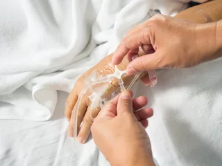 Fotobehang Close up nurse hand adjust set iv fluid intravenous drop saline drip in hospital room with blurry patient woman on hospital bed.Medical treatment emergency patient.Caregiver and hopeful concept.  © arcyto
