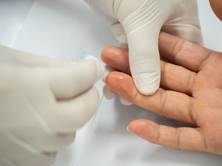 Naklejka premium Close up of nurse hand using lancet on finger to check blood sugar level with glucose meter at laboratory.Doctor measuring a patient's blood glucose.Human blood sugar test concept