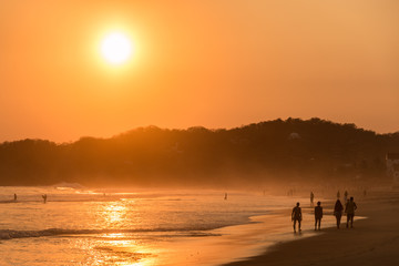 Fototapeta premium Magnifique couché de soleil sur la plage de Zipolite, Oaxaca, Mexique. Silhouettes de personnes marchant sur la plage en contre jour. 