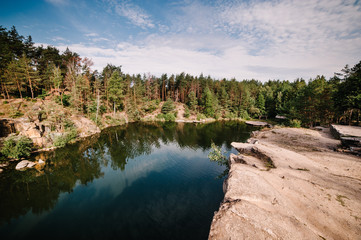 Obraz premium Landscape of an old flooded industrial granite quarry filled with water. Lake on the background of rocks and fir trees. Canyon. The nature of autumn. Place for text and design.