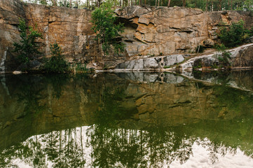 Reflection forests on lake on the background of rocks. Landscape of an old flooded industrial granite quarry filled with water. Canyon. The nature of autumn. Place for text and design.