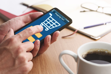 Online shopping. Shopping cart on smartphone display.Closeup of male hands touching smartphone screen at table.