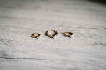 Wedding accessory bride. Stylish silver earrings, gold rings are isolated on table standing on wooden background. Side view.