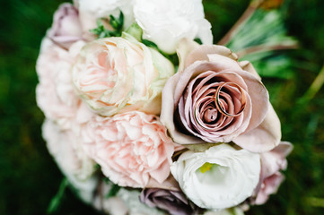Wedding rings bride and groom on the background bridal bouquet with gentle pastel flowers and pink roses and greenery lying on the grass. Autumn. flat lay. top view.