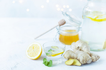 Healthy ginger drink in a cup. Ginger root, honey in a jar, lemon on a white table.