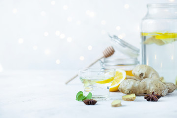 Healthy ginger drink in a cup. Ginger root, honey in a jar, lemon on a white table.