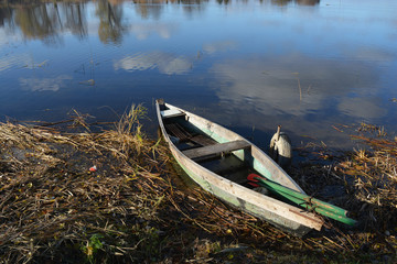 Lonely old wooden boat on lake coast and reflections