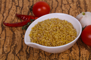 Raw bulgur in the bowl with tomatoes and garlic