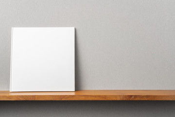 white square notebook on bookshelf and grey wall