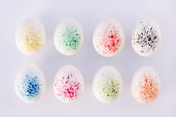 Easter eggs in their shells and paints are laid out on a white surface. White eggs in a spray of colored paints. Eggs laid out in a row and covered with decor watercolor paint.