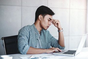 Tired and Stress Young Businessman Sitting on Desk in Office with Computer Laptop. Man Massaging a Nose and Closed Eyes, Keeping Calm and Relax from Hard Work